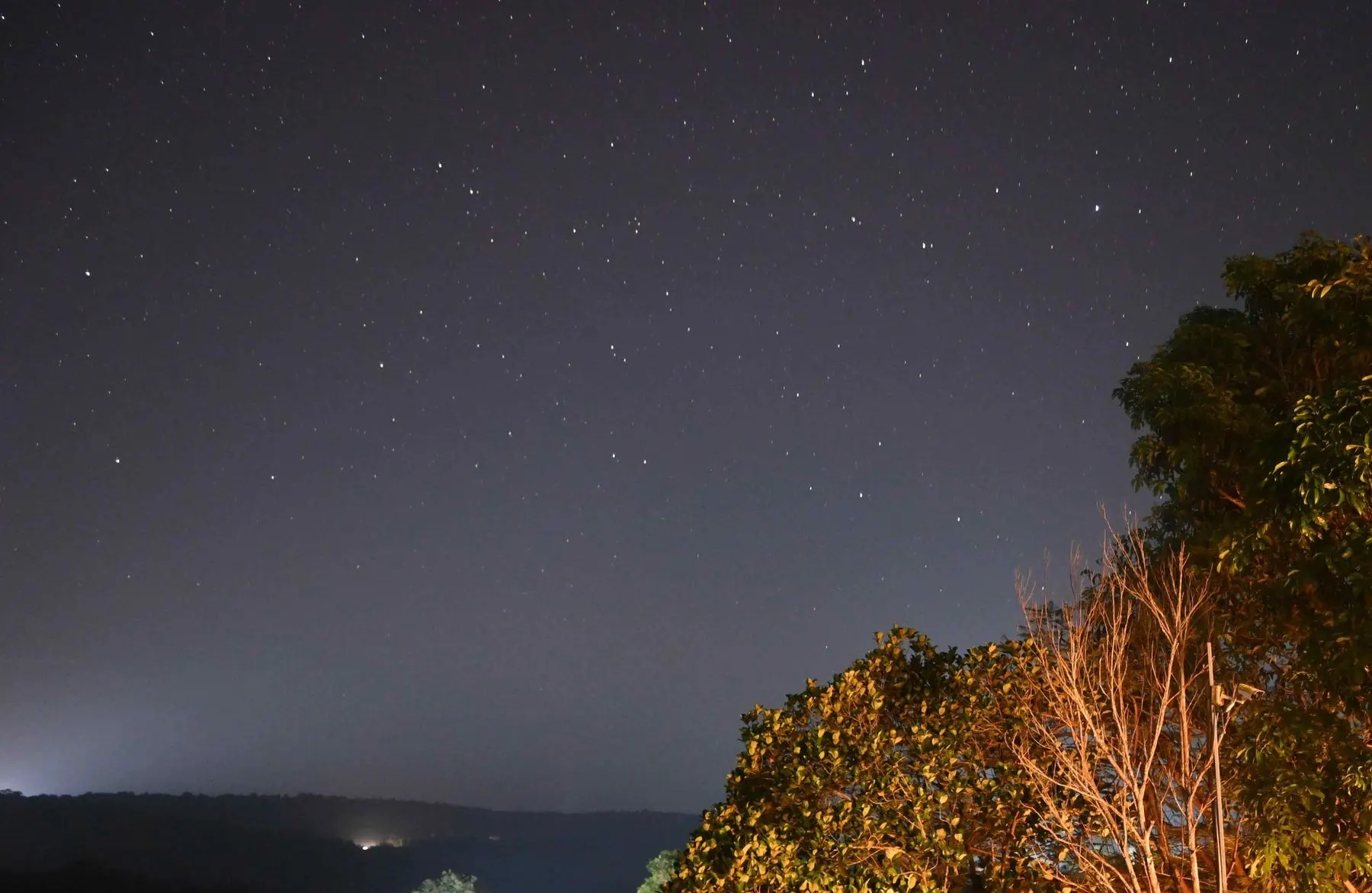 Long-exposure night sky over the Dapoli hills with lights on the horizon